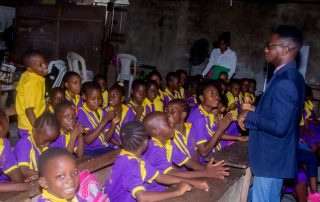 primary school children listening to a career talk from Tosin Ikuyiminu